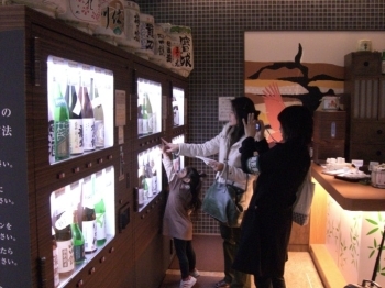 「空港銘酒蔵」の１００円試飲自販機。
ライターyasukaさんは、私の目を意識してか遠慮がちに一杯だけ。欲しがるお子様を叱り飛ばしながら。コンビのnonさんは本当に飲めないのか？