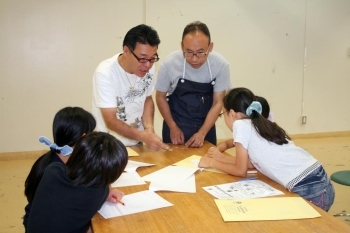 児童にイニシャル入りの銀の板を配る先生たち。