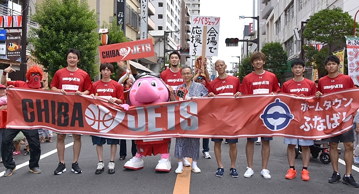 左から、マスク・ド・オッチー、荒尾岳選手、西村文男選手、ジャンボくん、小野龍猛選手、松戸徹船橋市長、阿部友和選手、上江田勇樹選手、石井講祐選手、原修太選手。後ろのプラカードはファンの有志！