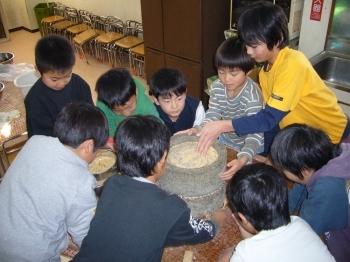 子どもたちが協力して炒りたて大豆を石臼で挽き、餅つき用のきな粉を作りました。