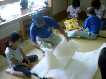 内海さんに、「綿入れ」を教わる子供。真剣な表情。綿を重ねて、折って、ちぎる。