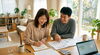 明るいリビングのテーブルで、設計図や資料を広げたご夫婦が、笑顔で未来の生活について語り合っている様子「八王子の工務店が教える！「後悔しない家を建てるための、アイディール流・家づくりガイド①相談・資金計画」」