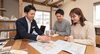 具体的な間取り図や総額の入った見積書を囲んで、分かりやすく真剣に、かつ温かい雰囲気で相談している様子「【コストのリアル】家づくりにかかる「総額」と資金計画の基本①坪単価より大切な「総額」の話」
