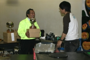 金属へら絞りの技術で作った優勝カップを授与する鍵屋さん（左）