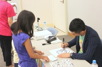イラストとサインを書くなばたさん（右）。なばたさんとこびとの話をする子どもは、本当に楽しそうでした。
