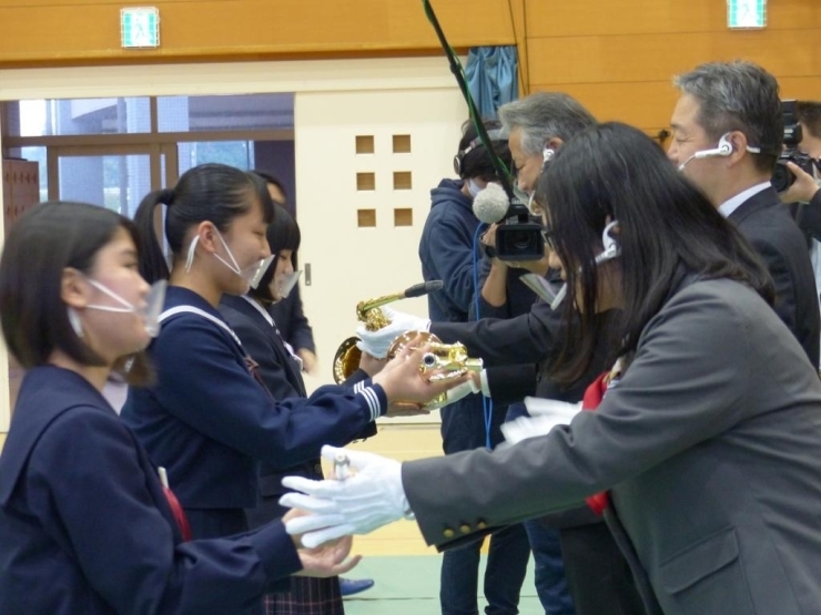 贈呈式には、行方市出身の小説家　額賀澪さん（手前　右）、鈴木市長（中央）、行方市学校教育長（奥）が出席し楽器を中学生に手渡しました。