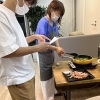 レシピの文字が小さすぎて見えないので、若手に読んでもらいながら調理するお母さん。