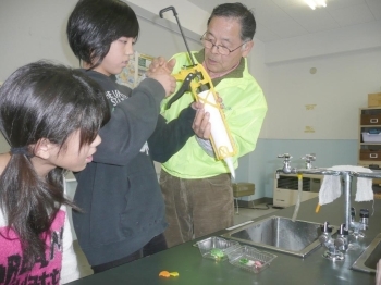 サンプルづくりの器具使用法を<br>教える田中さん