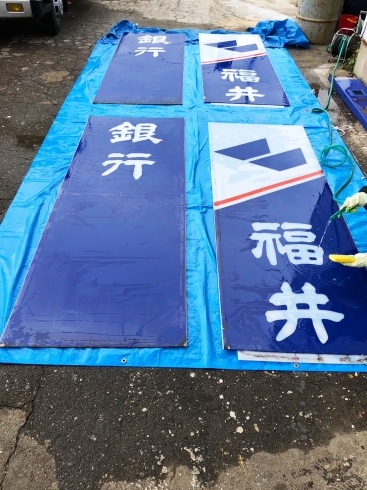 看板の表面を水洗いしている場面「福井銀行村国支店の看板修繕」